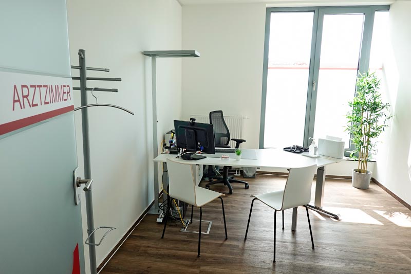 Ein modernes Büro mit einem Schreibtisch, Computern, Stühlen, einer Pflanze und einer Tür mit der Aufschrift "ARZTZIMMER".